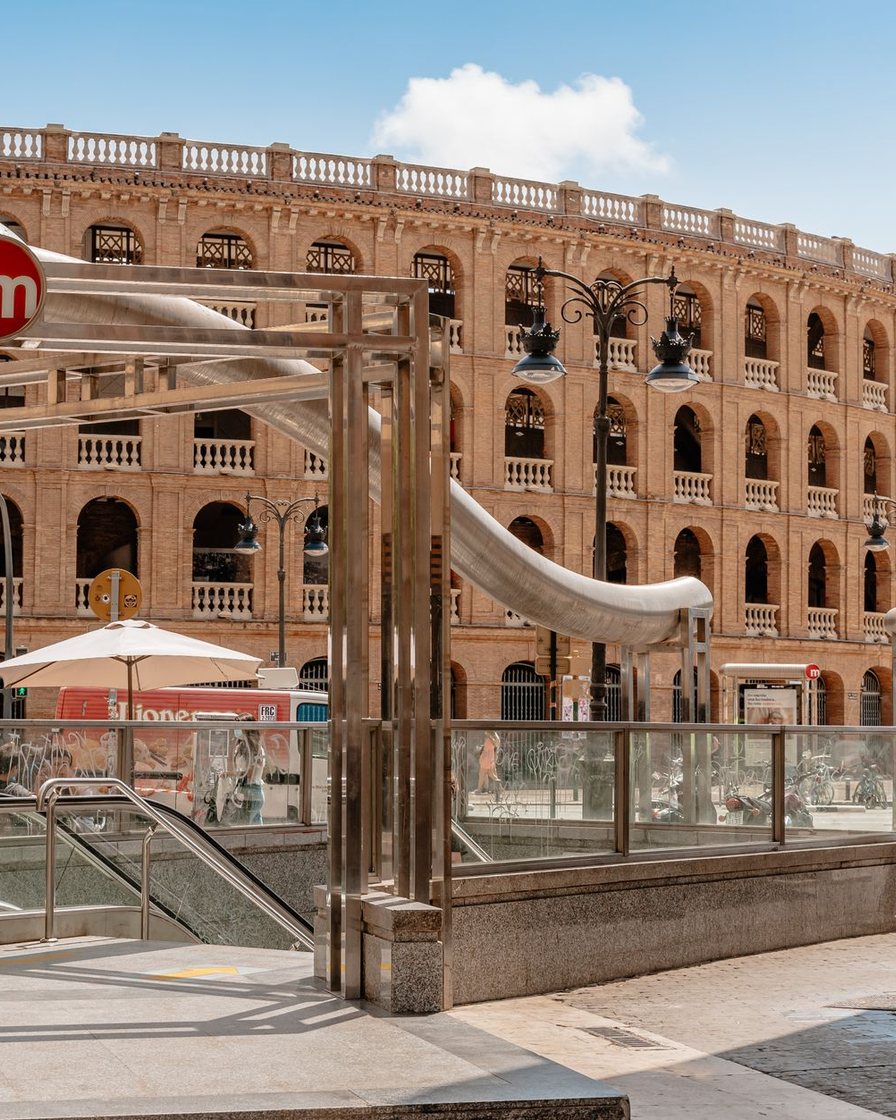 Andén subterráneo de una estación céntrica de Metrovalencia con paneles de horarios iluminados y pasajeros esperando junto a las puertas del tren