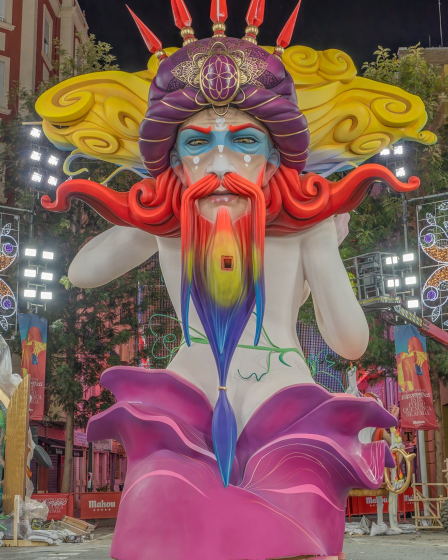 Artista fallero pintando la cabeza de un ninot de gran tamaño en un taller de la Ciutat de l'Artista Faller de Valencia, rodeado de figuras a medio hacer